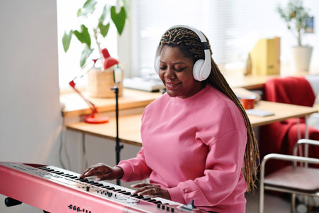 African American woman in wireless headphones playing piano sitting in her roomの写真素材