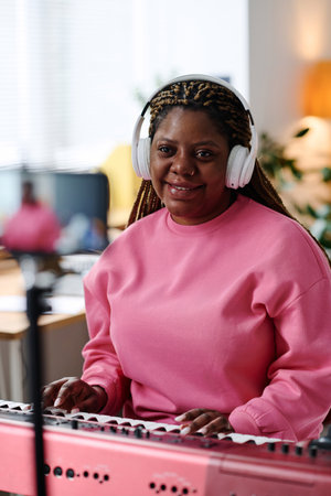 Vertical of African American girl in headphones smiling at camera while playing pianoの写真素材