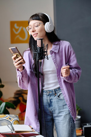 Young woman in headphones using her smartphone to sing song in microphoneの写真素材