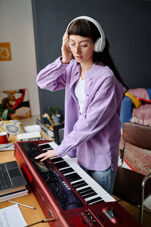 Young woman in headphones playing piano to record song during rehearsal in studioの写真素材
