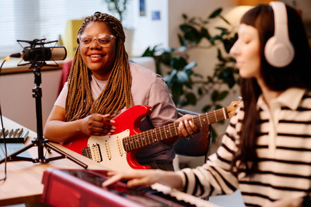 African American woman playing guitar and recording song together with her friend while she playing pianoの写真素材