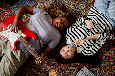 High angle view of happy friends singing songs and playing guitar while lying on the floor at homeの写真素材