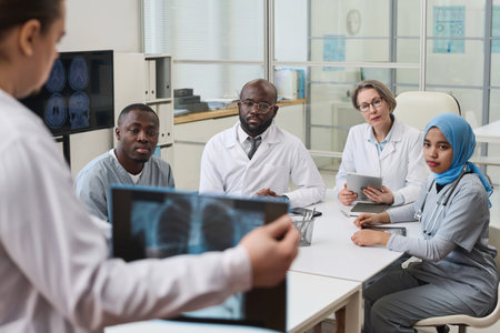 Doctor showing x-ray image of lungs to his colleagues and discussing disease with them during teamwork in officeの写真素材