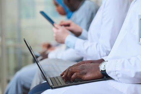 Close-up of African American doctor in white coat typing on laptop at conference