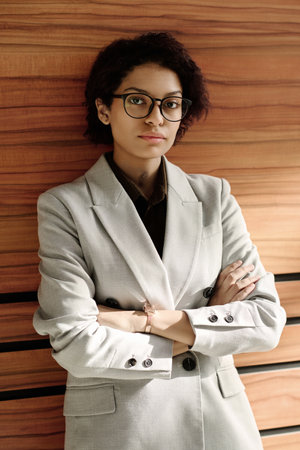 Portrait of young businesswoman in eyeglasses and white suit standing with her arms crossed and looking at cameraの写真素材