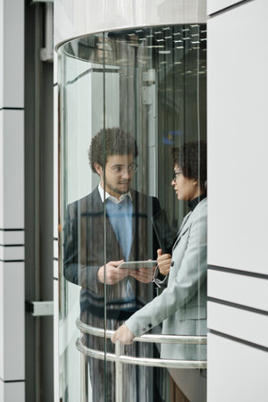Vertical image of business couple using digital tablet and talking during their meeting in elevator...