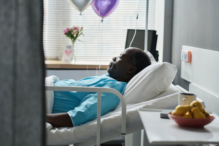 African American man sleeping on bed while having treatment in hospital wardの写真素材