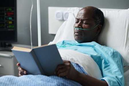 African American elderly patient reading book while lying in ward during his rehabilitationの写真素材