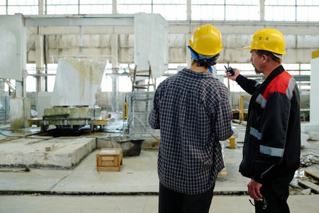 Rear view of foreman pointing at machine and giving task to worker in stone cutting plant