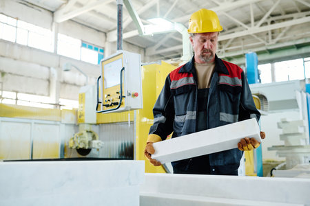 Worker in uniform putting piece of stone on machine for cutting during his work in plant