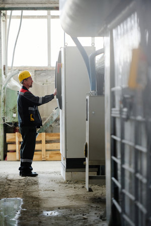 Vertical image of engineer in uniform setting the work of machine with computer in workshop