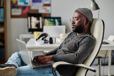 African American developer working with software on laptop while sitting on chair in officeの写真素材