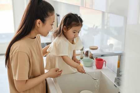 Young mom teaching her daughter to wash dishes in the kitchenの写真素材