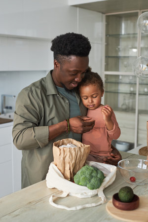 Vertical image of African American dad with little daughter standing in the kitchen