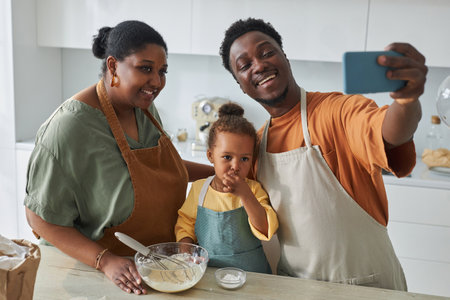 Happy African American family making selfie portrait on smartphone while cooking together in the...