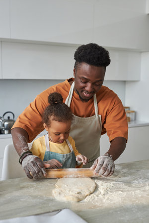 African American dad rolling dough together with his child in the kitchen