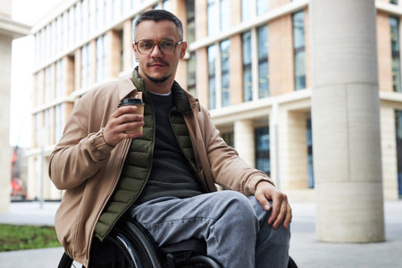 Portrait of young man with disability looking at camera while drinking coffee in the cityの写真素材