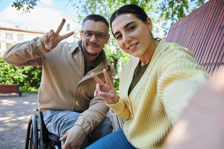 Selfie portrait of young woman posing at camera together with her friend with disability outdoorsの写真素材