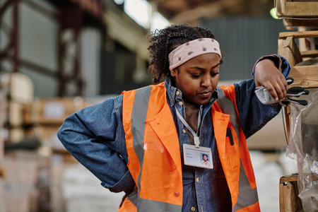 African American warehouse worker standing near the pallet with containers and resting after work