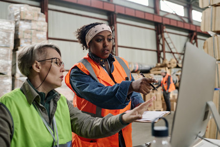 Foreman pointing at monitor and discussing document online with worker during their work in warehouseの写真素材