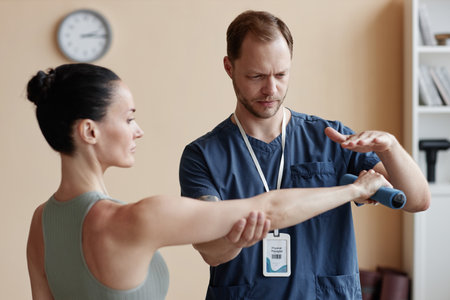 Young woman training with dumbbells together with therapist during her rehabilitation in hospitalの写真素材