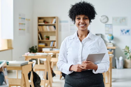 Portrait of young African American teacher with tablet pc smiling at camera while standing in classroomの写真素材