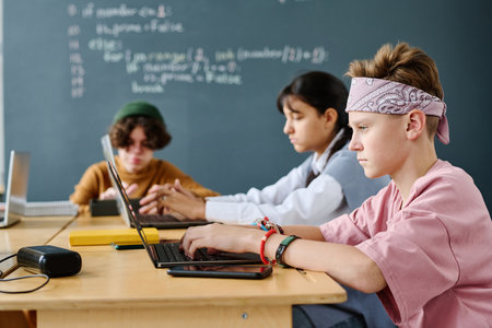 Group of children studying IT using computers while sitting in the classroomの写真素材