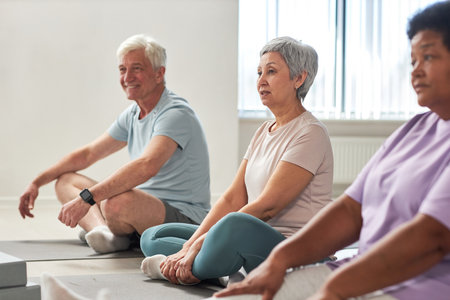 Group of people sitting on exercise mats and exercising together in yoga studioの写真素材