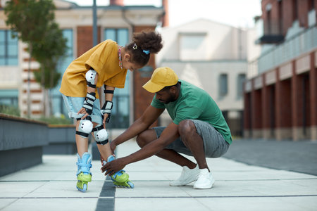 African American father helping his daughter to wear roller skates during their walk outdoorsの写真素材