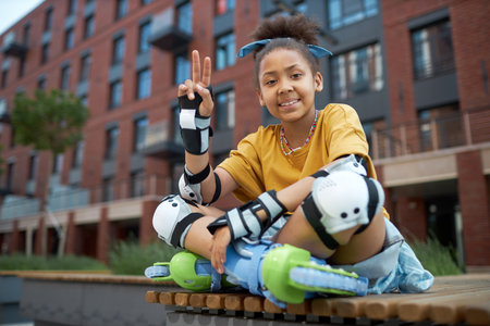 Portrait of African American girl in roller skates sitting on bench and smiling at camera outdoorsの写真素材