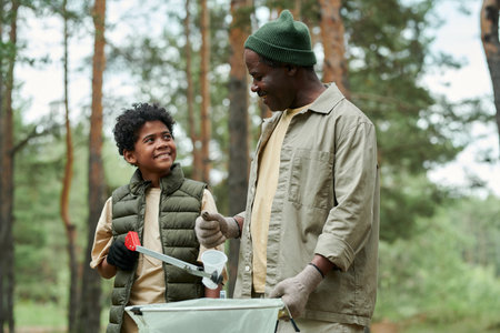 African American dad picking up garbage together with his son in the forestの写真素材
