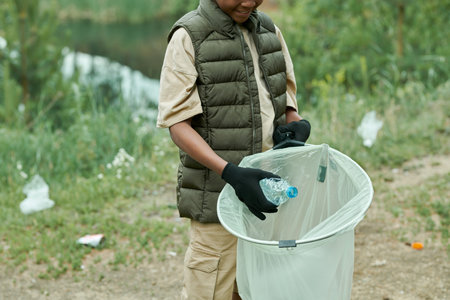 Close-up of African American boy picking up garbage in bag outdoors