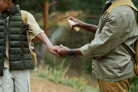 Dad protecting his son from insects using spray during their hiking in the forest