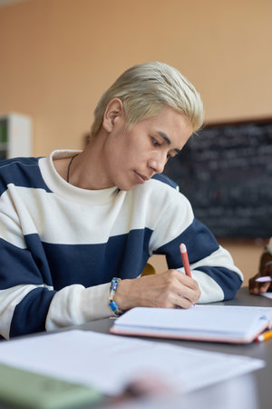 Young serious student in casualwear looking at copybook page while making notes or writing down...