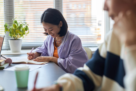 Happy young Asian brunette woman looking through test questions on paper at lesson while keeping...