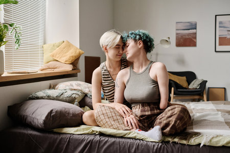 Young lesbian couple sitting on bed in bedroom and enjoying each otherの写真素材