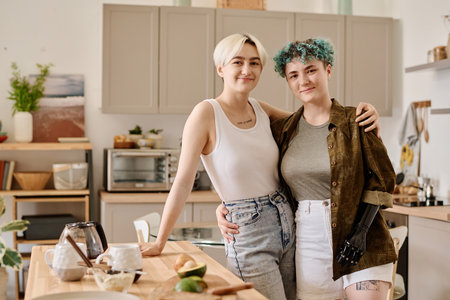 Portrait of young lesbian couple embracing and looking at camera while preparing food in the kitchenの写真素材