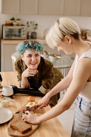 Vertical image of girlfriends having fun and talking to each other while preparing food in the kitchenの写真素材