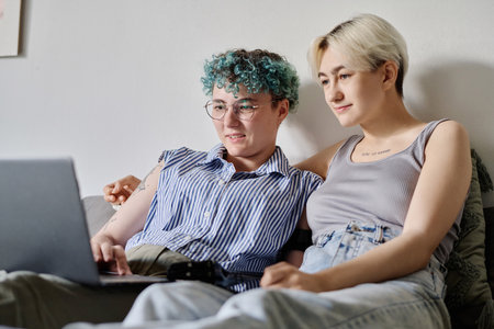 Lovely lesbian couple relaxing in bedroom and watching movie on laptopの写真素材