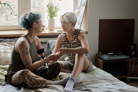 Lesbian girls sitting on bed and talking to each other, they spending time at home