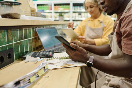 Colleagues sitting at table and using calculate and computer to control the sale of goods in...