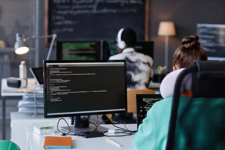 Rear view of young people sitting at their workplaces with computers and working with programの写真素材