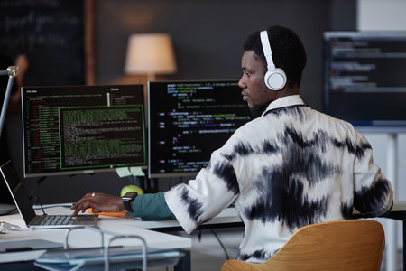 Young African American programmer in wireless headphones working with security codes at his workplace in IT officeの写真素材