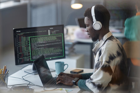 African American programmer in headphones typing on laptop at his workplaceの写真素材