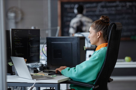 Young woman sitting at her workplace in front of computer monitor and developing new softwareの写真素材