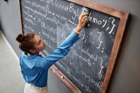High angle view of young IT teacher wiping text from the blackboard in the classroom