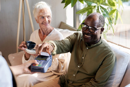 Smiling African American man paying for coffee with credit card while sitting in cafe with his wifeの写真素材