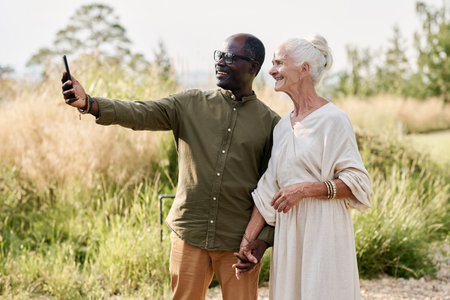 Senior couple making selfie portrait on smartphone while walking outdoorsの写真素材