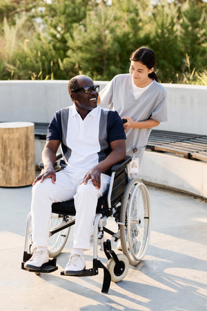 Vertical image of caregiver walking outdoors with senior man with disabilityの写真素材