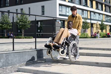 Man helping his friend in wheelchair to go down the stairs during their walk in the city